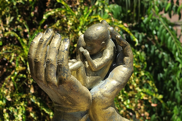 Skulptur zeigt sehr kleines Kleinkind in den Händen eines Menschen
