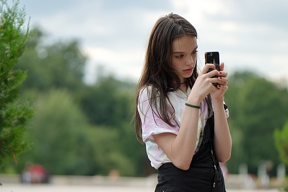 Mädchen schaut konzentriert auf Smartphone in seinen Händen