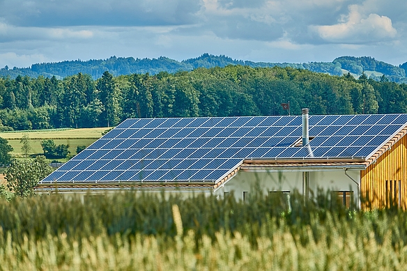 Modernes Betriebsgebäude aus Holz mit Photovoltaik vor idyllischer Landschaft mit Wald auf Hügeln